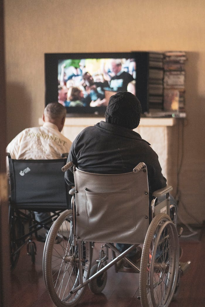Two adults in wheelchairs watching television, creating a cozy and inclusive atmosphere indoors.